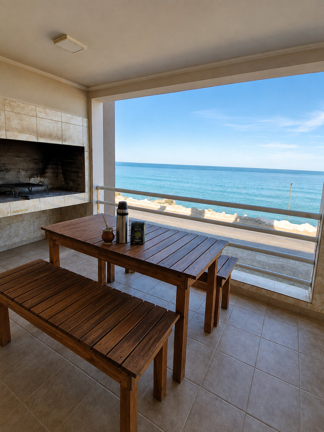 Balcón con mesa, bancos y parrilla frente al mar
